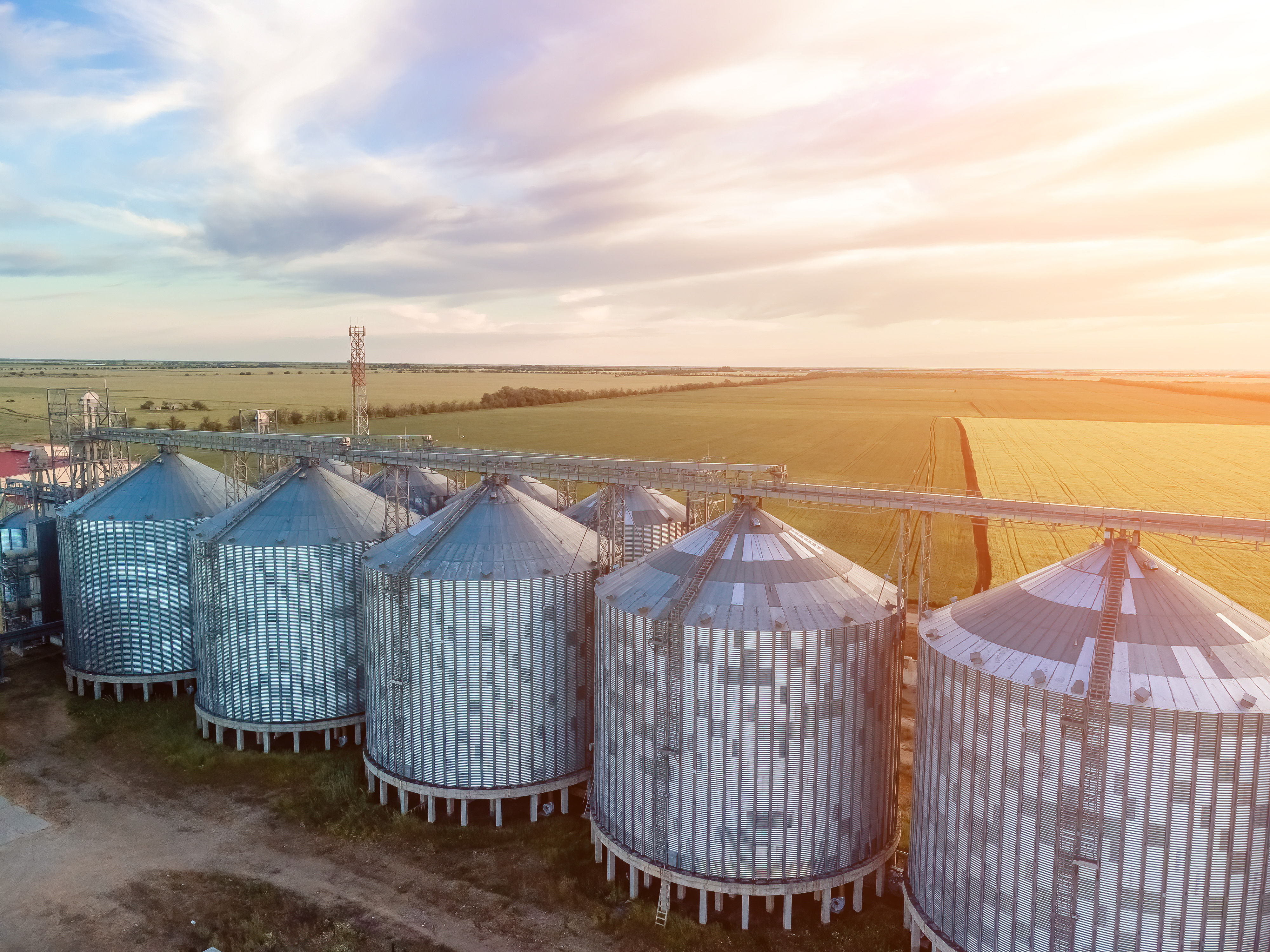Aerial view of grain silos beside a golden field at sunset